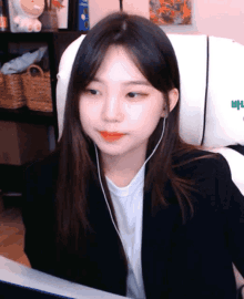 a girl wearing ear buds is sitting in front of a white chair with the letter b on it