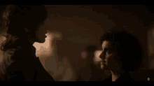 a woman and a boy are looking at each other in a dark room with an o on the bottom right corner