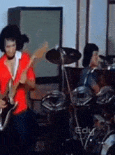 a man in a red shirt is playing a guitar and a man in a black shirt is playing drums .