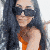 a woman with long black hair wearing sunglasses and an orange top