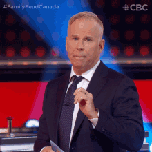 a man in a suit and tie holds a piece of paper in front of a cbc logo