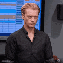 a man in a black shirt is standing in front of a monitor .