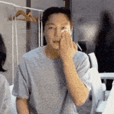 a man in a grey shirt wipes his face with a tissue