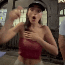 a woman wearing a hat and a red crop top is standing in front of a building that says stac