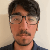 a man with glasses and a beard looks at the camera .