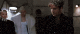 a man in a black suit is standing next to a woman in a white coat in a dark room .