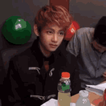 a young man is sitting at a table with bottles of soda and a bowling ball .