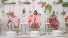 a woman in a pink fur coat is sitting in a chair next to two other women