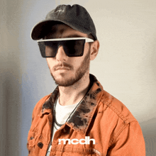 a man wearing sunglasses and a hat has the word mcdh on his jacket