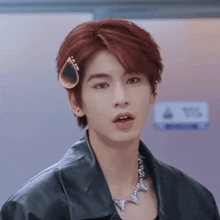 a young man with red hair is wearing a black jacket and necklace