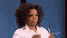 a woman with curly hair is wearing a white shirt and holding a piece of paper in her hand .