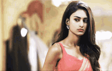 a woman wearing a pink top and earrings stands in front of a wall