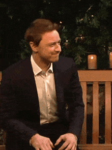 a man in a suit is sitting on a bench with his hands on his hips .