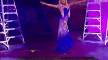 a woman in a blue dress is dancing on a stage in front of ladder .