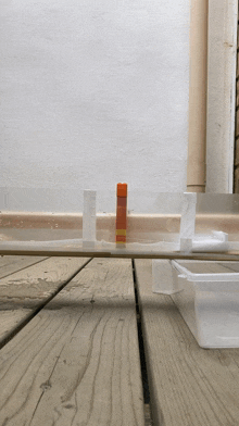 a bottle of glue is sitting on a wooden table next to a plastic container