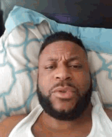 a man with a beard is laying in bed with a pillow on his head .