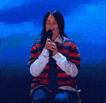 a woman singing into a microphone while wearing a striped shirt