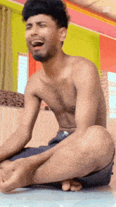 a shirtless man sits on the floor with his legs crossed and laughs
