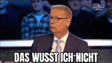 a man in a suit and tie is sitting in front of a crowd and says das wusst ich nicht .