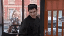 a man in a black jacket is standing in front of a door with a sign on it .