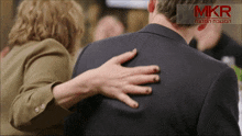 a woman 's hand rests on a man 's shoulder with a mkr logo in the background