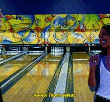 a woman is standing in front of a bowling alley with the words ha-ha that 's defeat written on the screen .