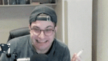 a man wearing glasses , a hat and a beanie is sitting in a chair .