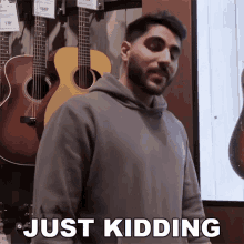 a man is standing in front of a wall of guitars and the word just kidding is on the screen