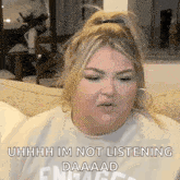 a woman is sitting on a couch wearing a sweater that says `` uhhhh im not listening daaaad '' .