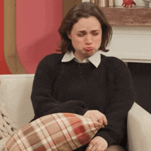 a woman sitting on a couch with a plaid pillow making a face