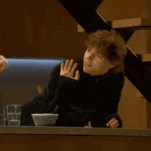 a man in a black sweater is sitting at a counter with a bowl of food
