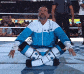 a wrestler in a blue and white outfit sits on the ground