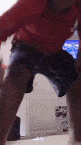 a man in a red shirt and blue shorts is standing in front of a tv