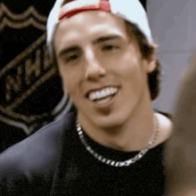 a man wearing a hat and a necklace is smiling in front of a nhl banner