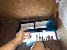 a person 's hand is reaching out towards a window with bottles of shampoo on it