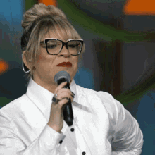 a woman wearing glasses holds a microphone in her hand