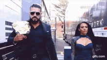 a man in a suit is holding a wrestling championship belt next to a woman in a blue dress .