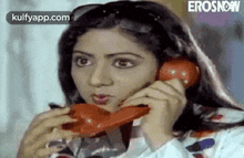 a woman is talking on a red telephone and looking at the camera .