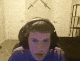 a young man wearing headphones looks at the camera with two swords on the wall behind him