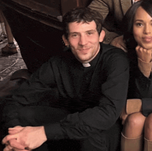 a man in a black shirt with a white cross on his collar sits next to a woman