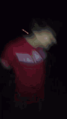 a blurry picture of a man in a red shirt making a funny face in the dark .