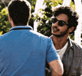 a man wearing sunglasses and a blue shirt is talking to another man
