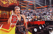 a woman is holding a wrestling championship belt in front of a crowd at a wrestling event