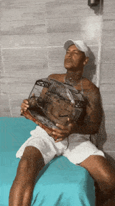 a man sitting on a bed holding a bird cage with a box that says ' o'clock ' on it