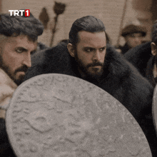 a man in a fur coat holds a shield in front of a sign that says trt1