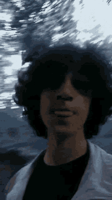 a young man with curly hair and sunglasses looks at the camera