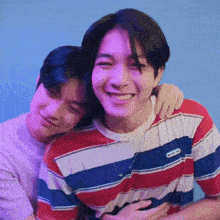 two young men are hugging each other and smiling for the camera while wearing striped shirts .