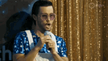 a man wearing sunglasses is singing into a microphone in front of a gold curtain with the number 10 on it