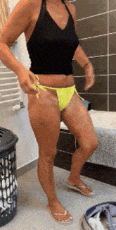 a woman in a black tank top and yellow bikini bottoms is standing in a bathroom