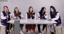 a group of girls in varsity jackets are sitting around a table .